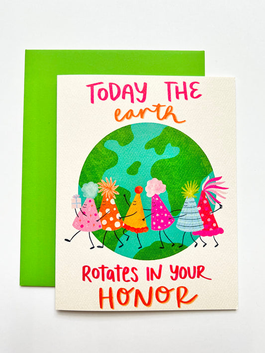 Card with cartoon characters of birthday hats around the Earth and text 'Today the Earth Rotates in Your Honor' on a white background.