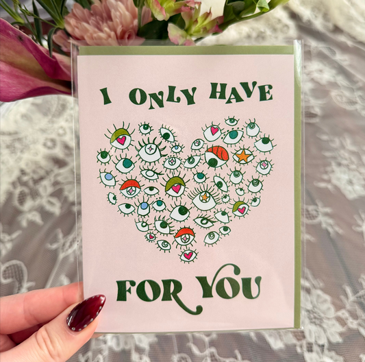 Hand holding a card with illustration of eyes in the shape of a heart saying "i only have eyes for you"