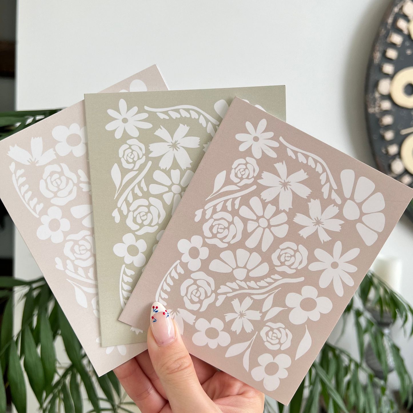 Hand holding three floral patterned cards with a white background