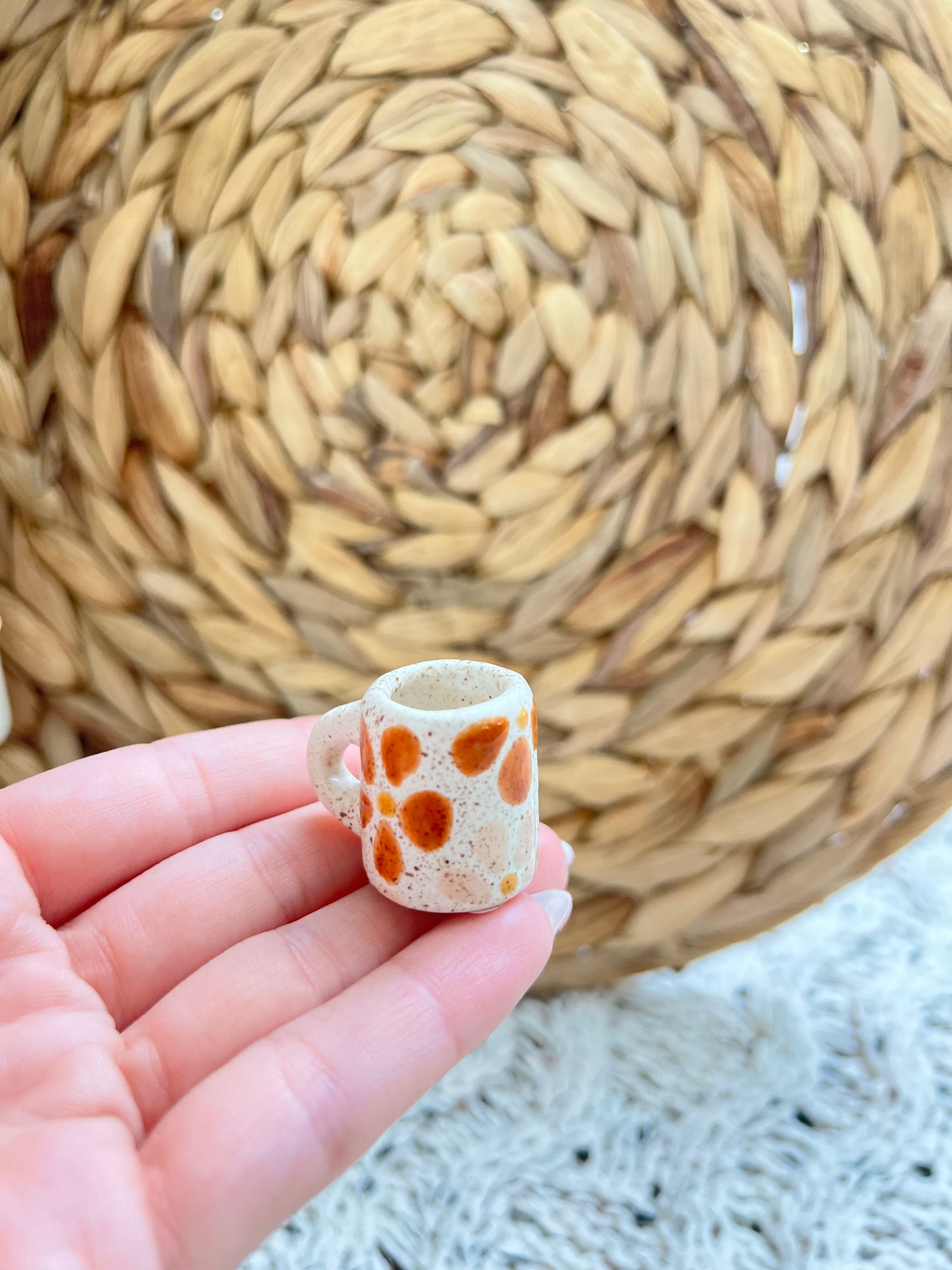 Small ceramic cup with orange patterns held in a hand against a woven mat background