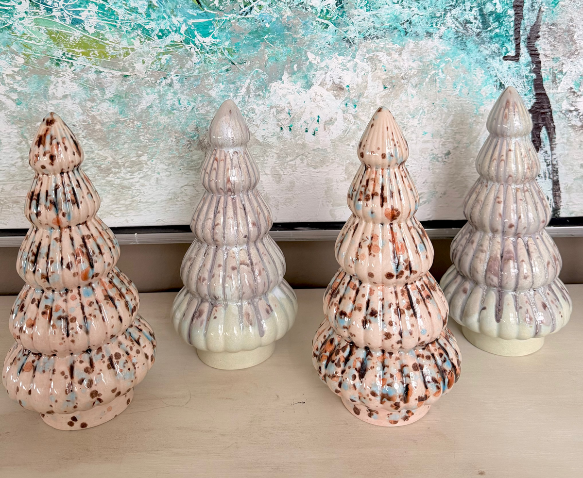 Four decorative tree sculptures on a surface with a colorful abstract painting in the background.