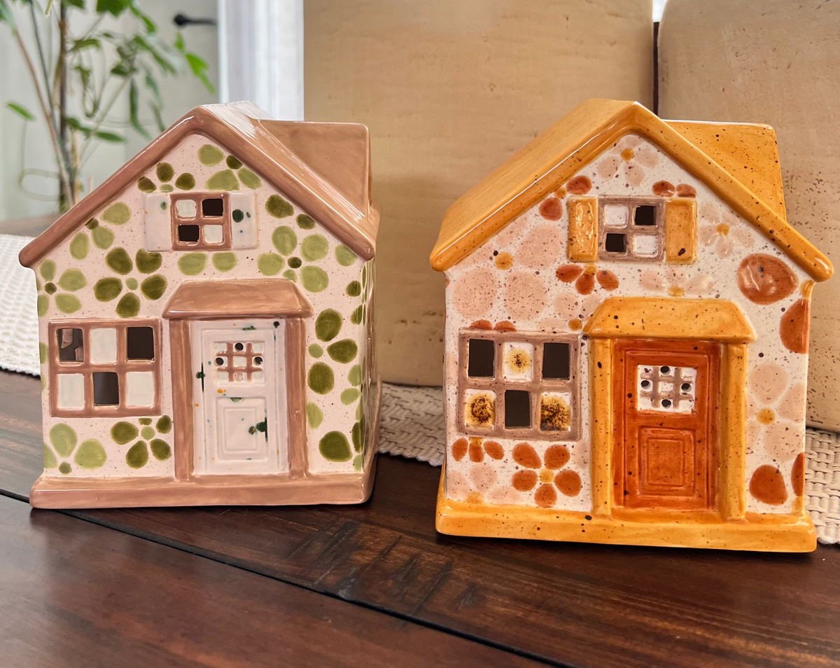 Two decorative ceramic houses on a wooden surface with a large vase in the background.