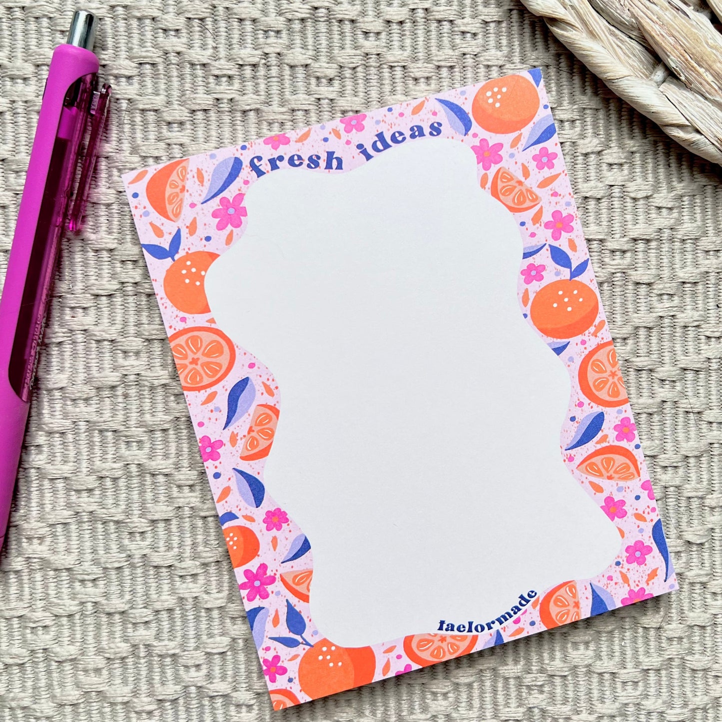 Notepad with colorful fruit design and a pen on a textured surface