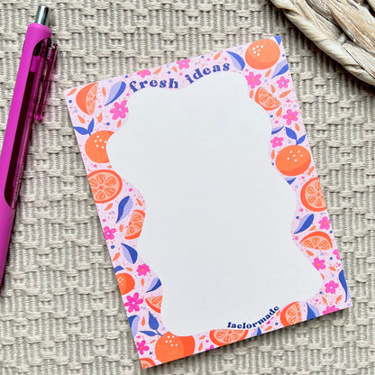 Notepad with colorful fruit design and a pen on a textured surface