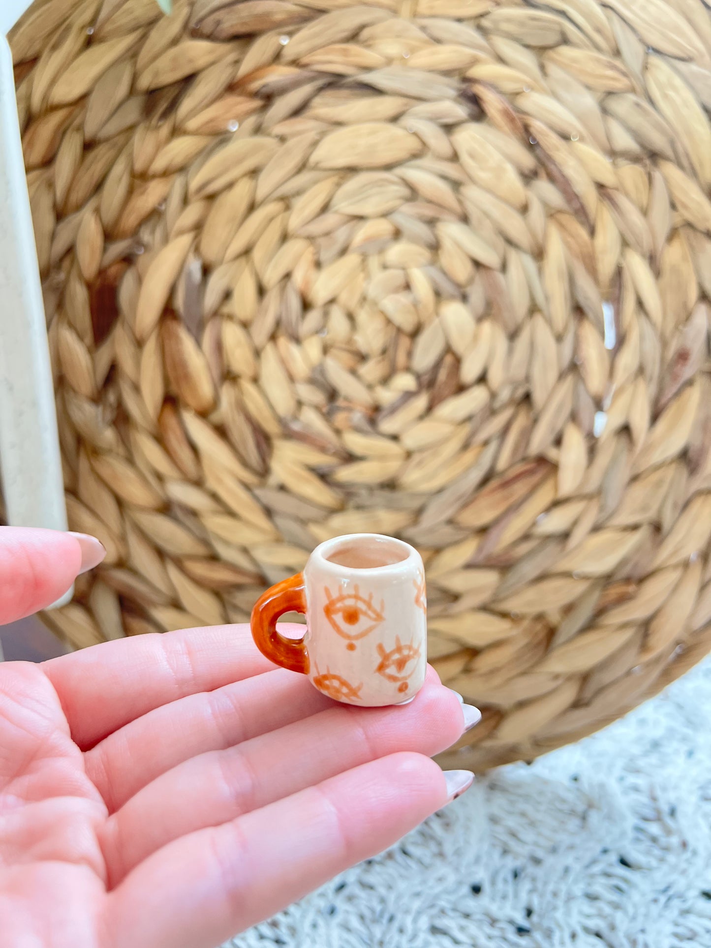Small ceramic cup with eye design held in a hand against a woven mat background