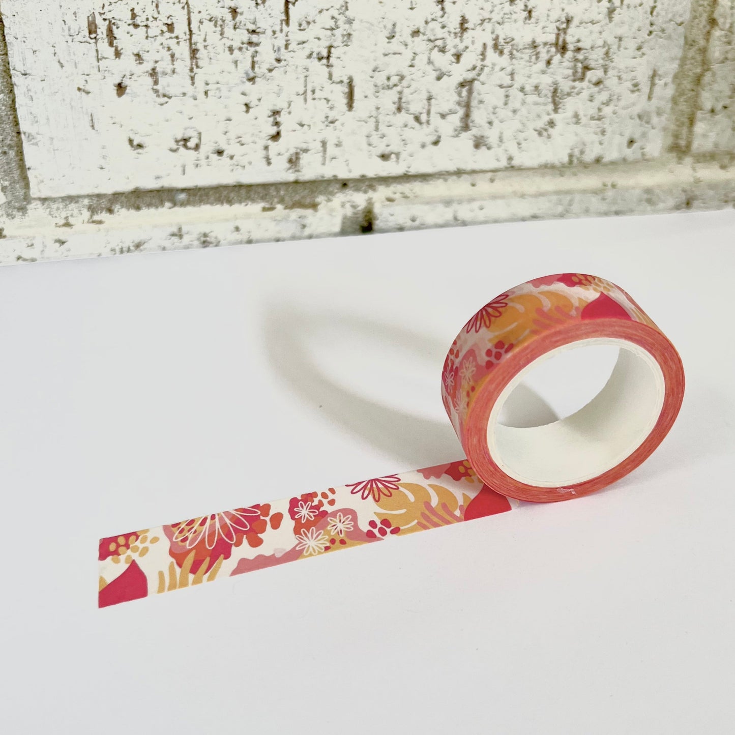 Roll of floral-patterned tape on a white surface with a brick wall background