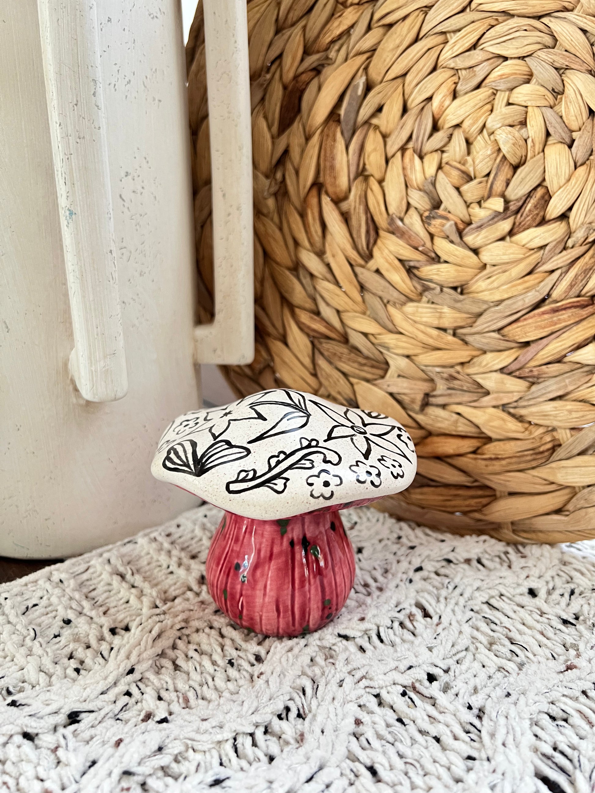 Decorative ceramic mushroom with black floral design on a pink base, placed on a textured surface.