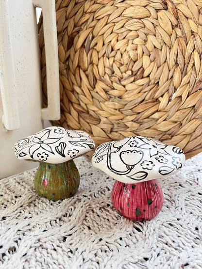 Two decorative ceramic mushrooms with black line art on a textured surface.