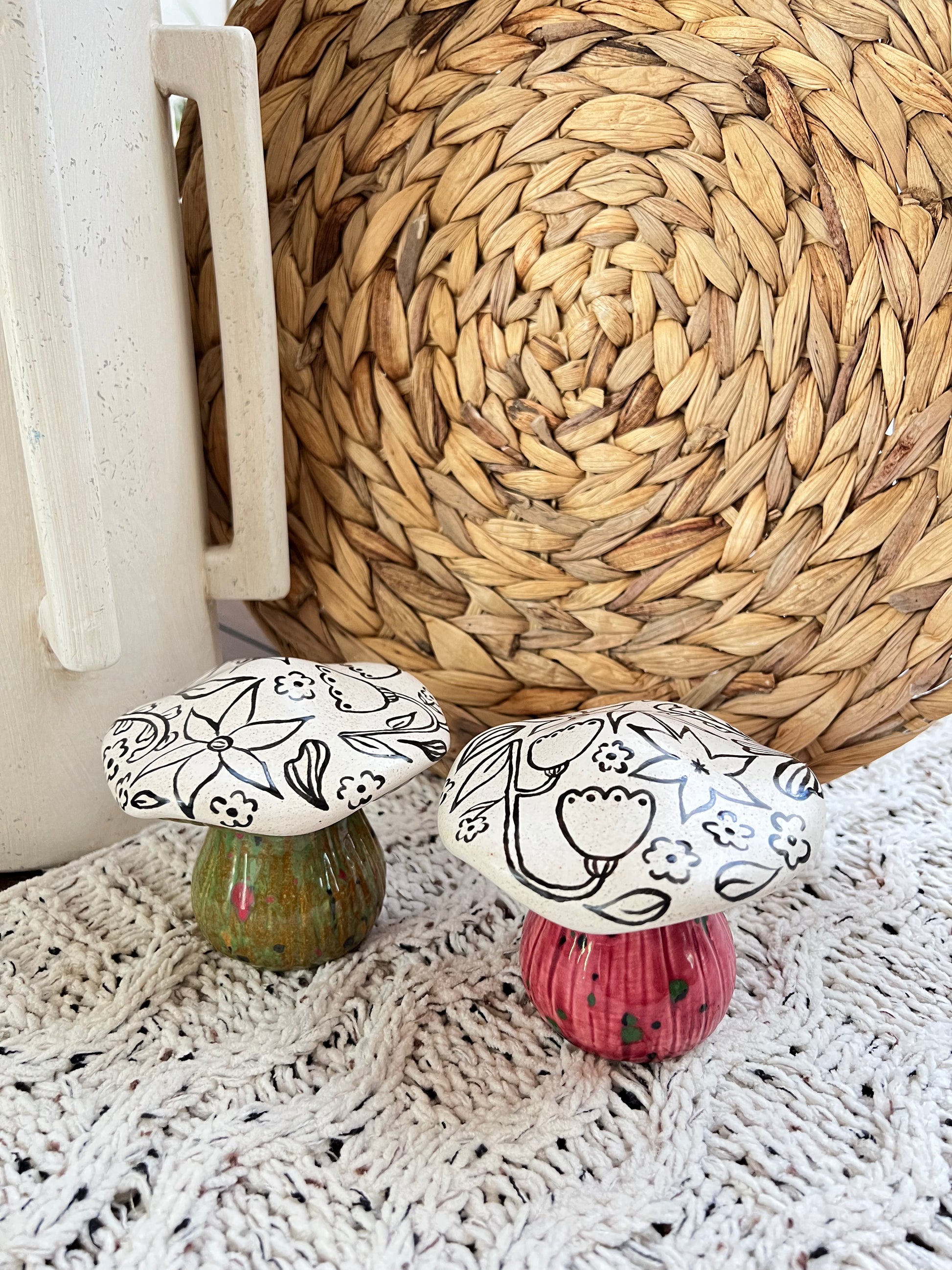 Two ceramic mushrooms with floral patterns on a textured surface.
