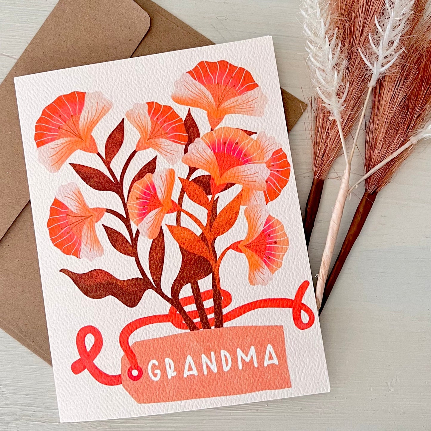 Greeting card with floral design and 'Grandma' text on a wooden surface with dried plants.