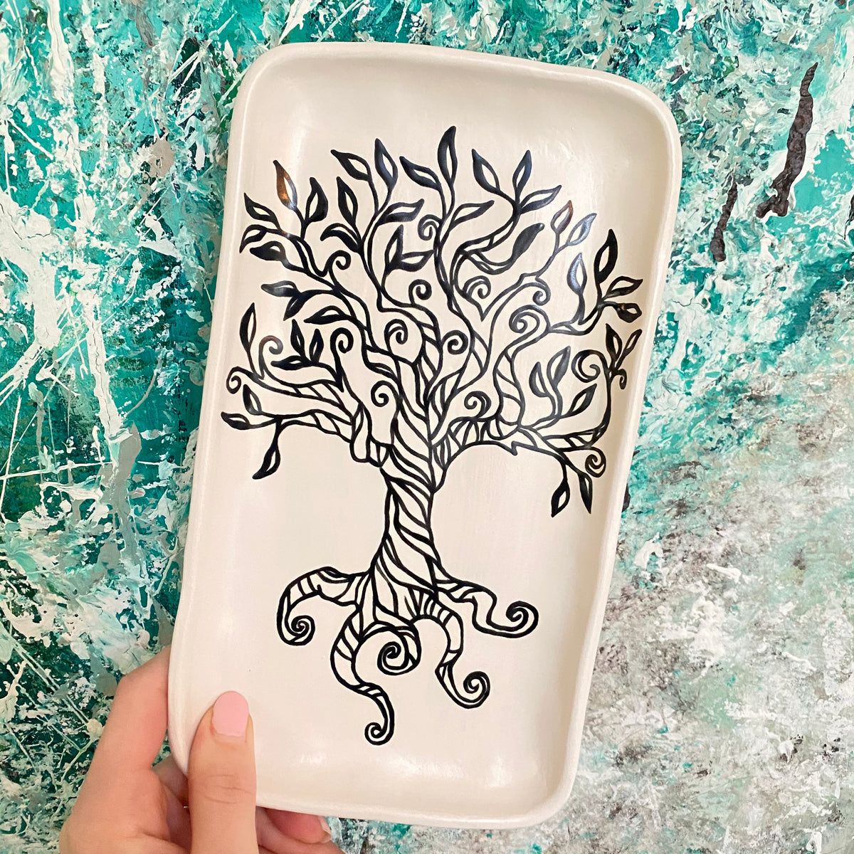 White rectangular plate with black tree design held against a textured blue and gray background