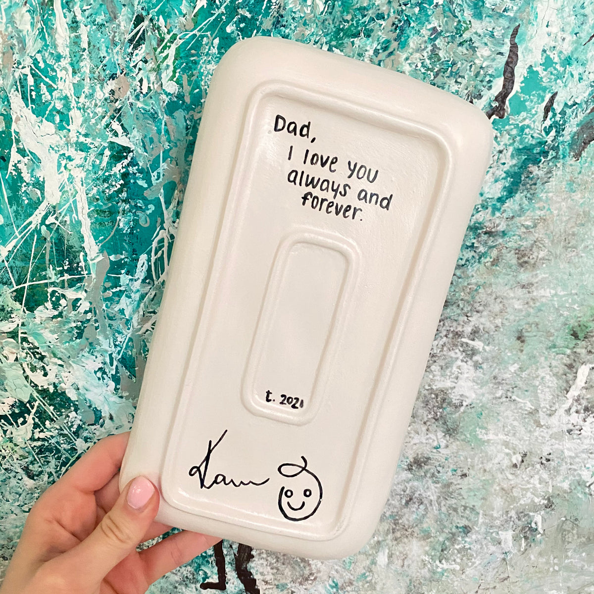 Hand holding a white rectangular tray with message on a textured blue and green background