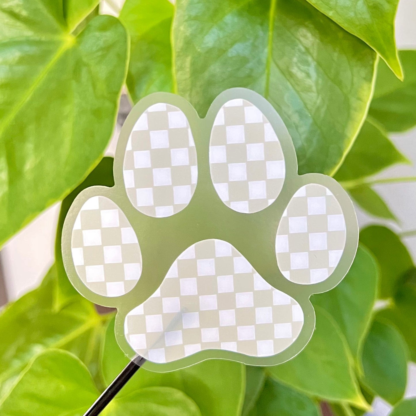 Clear paw-shaped sticker with checkered pattern on green leaves