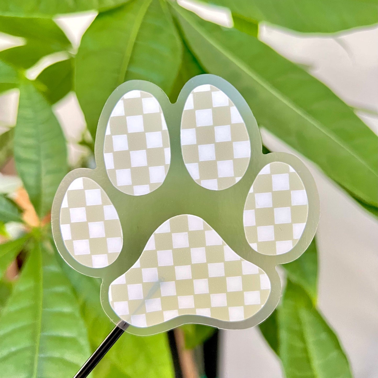Checkered paw print sticker on a green background with leaves.