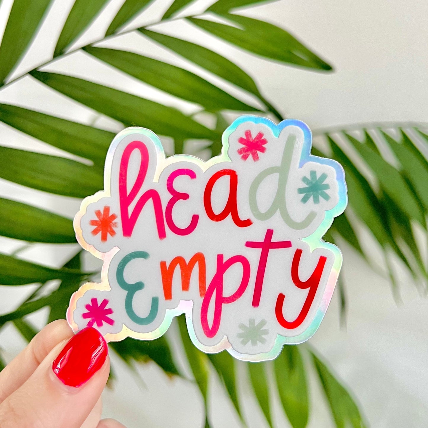 Holographic sticker with 'head empty' text held by a hand against a leafy background