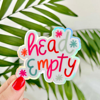 Holographic sticker with 'head empty' text held by a hand against a leafy background