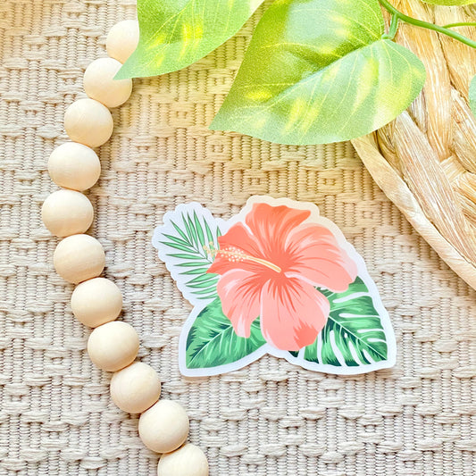 Sticker of a pink flower with green leaves on a woven surface with wooden beads and leaves.