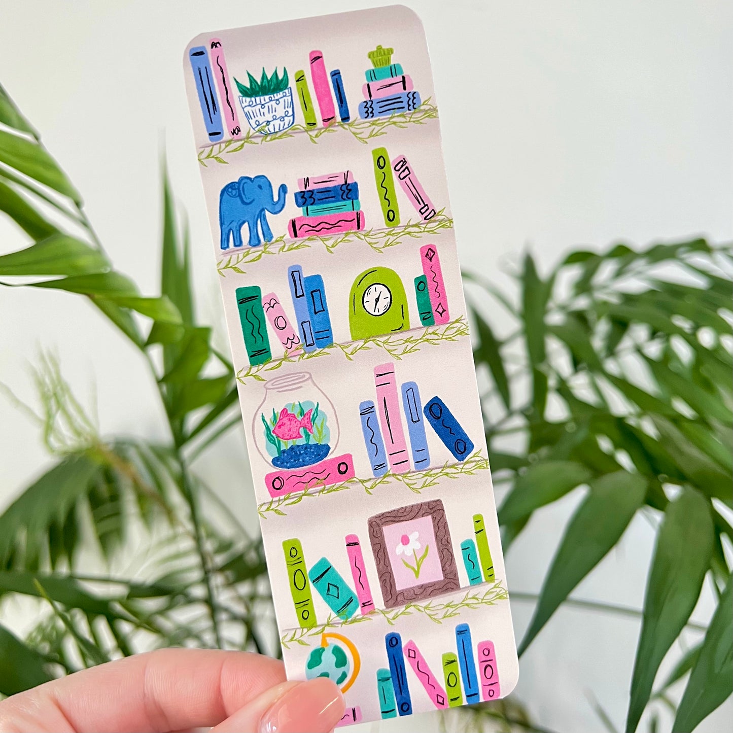 Illustration of a bookshelf on a bookmark held by a hand against a green leafy background