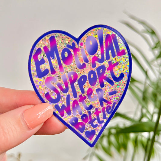 Heart-shaped holographic sticker with 'Emotional Support Water Bottle' text held by a hand against a light background.