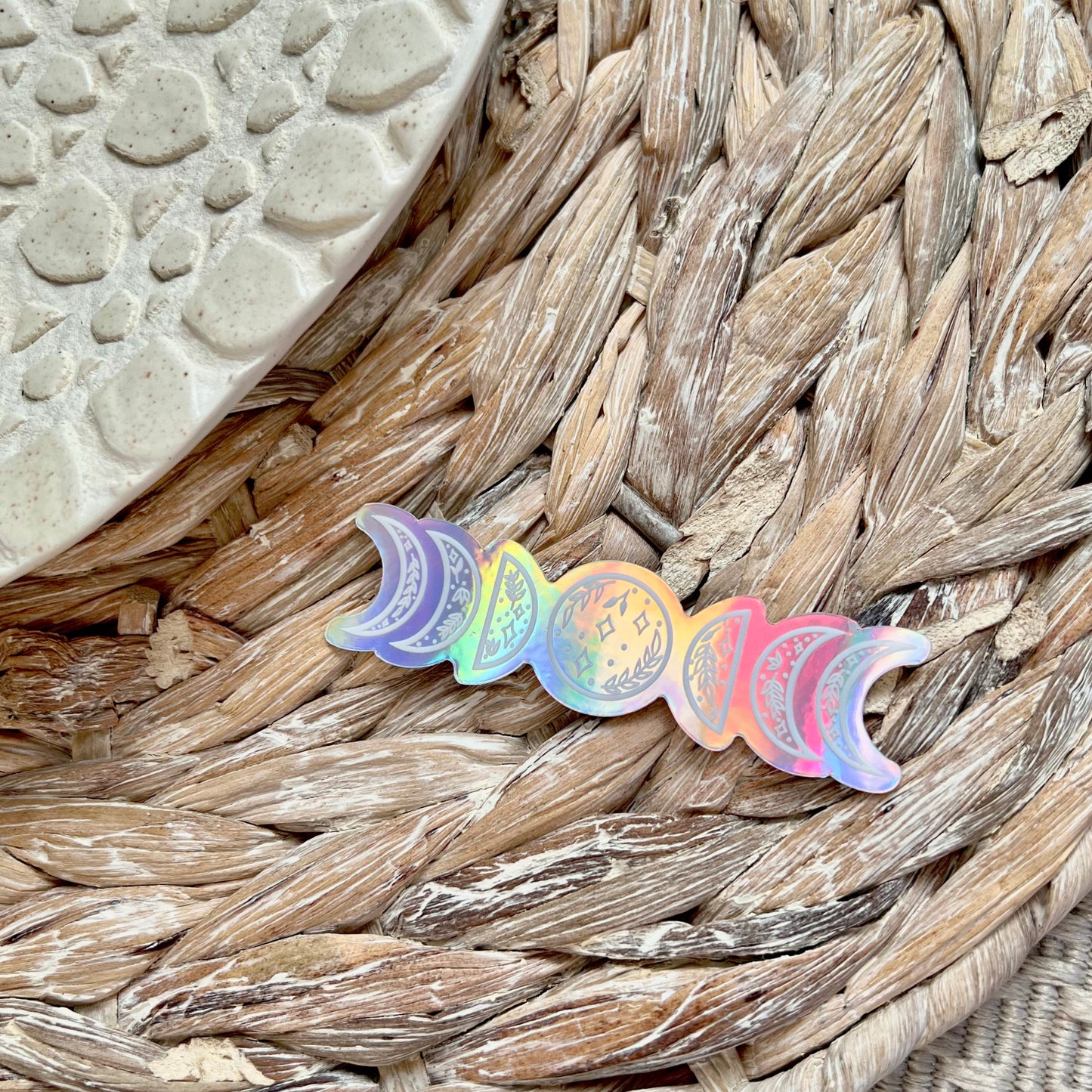 Holographic moon phase sticker on a textured woven surface