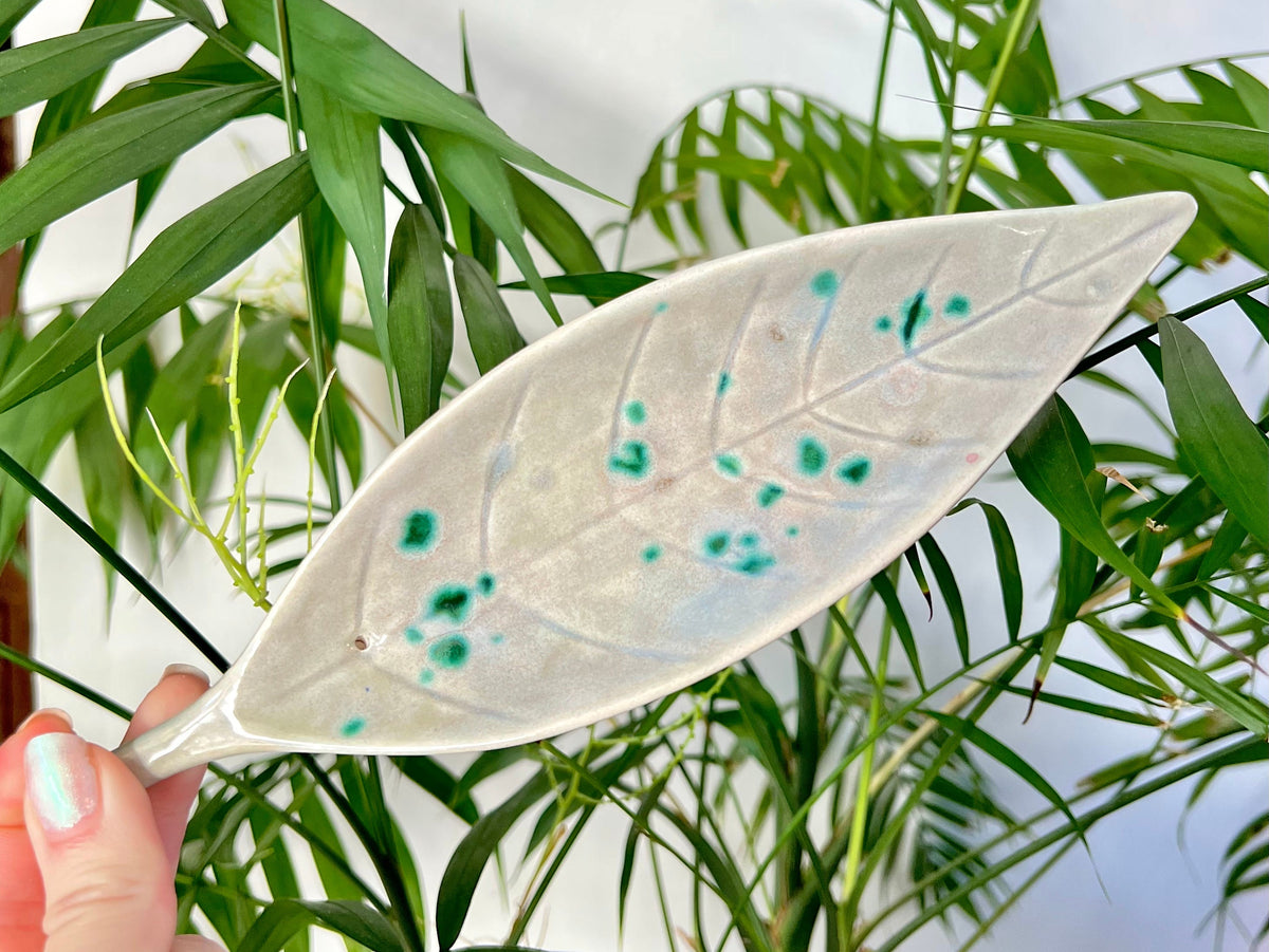 White ceramic leaf with green speckles held in front of green plants