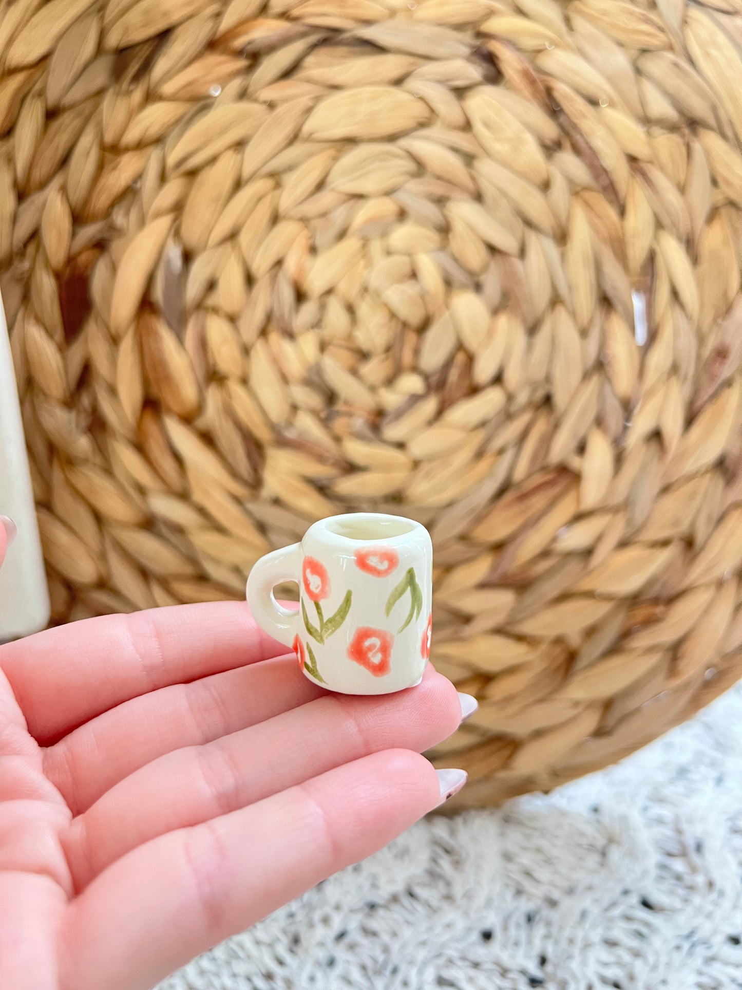 Small ceramic cup with floral design held in a hand against a woven mat background