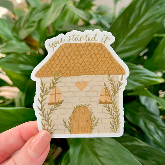 House-shaped sticker with 'you started it' text held against a green leafy background