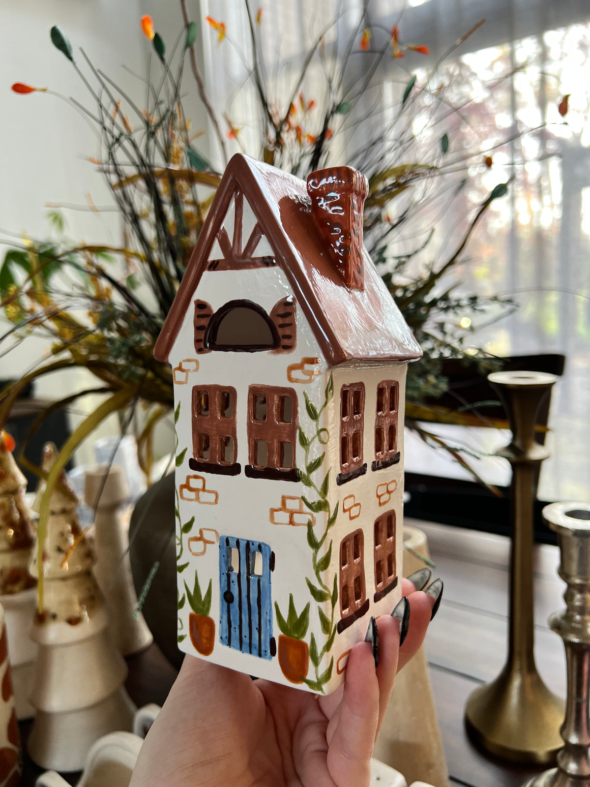 Ceramic decorative house with a white roof and brown walls, surrounded by blurred indoor decor.