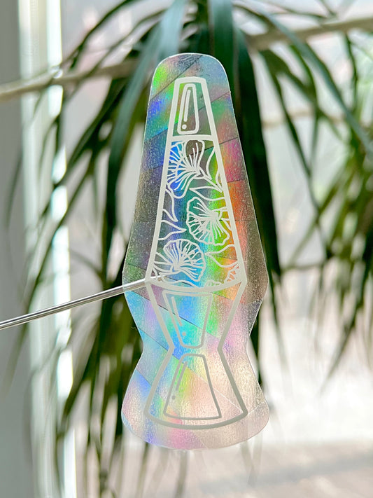 Iridescent lava lamp with floral design against a blurred plant background