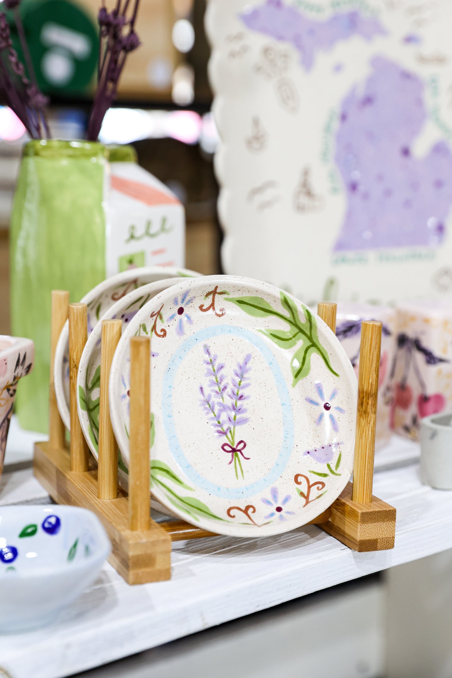 Decorative ceramic dishes with floral designs on a wooden stand, with a blurred background of other decorative items.
