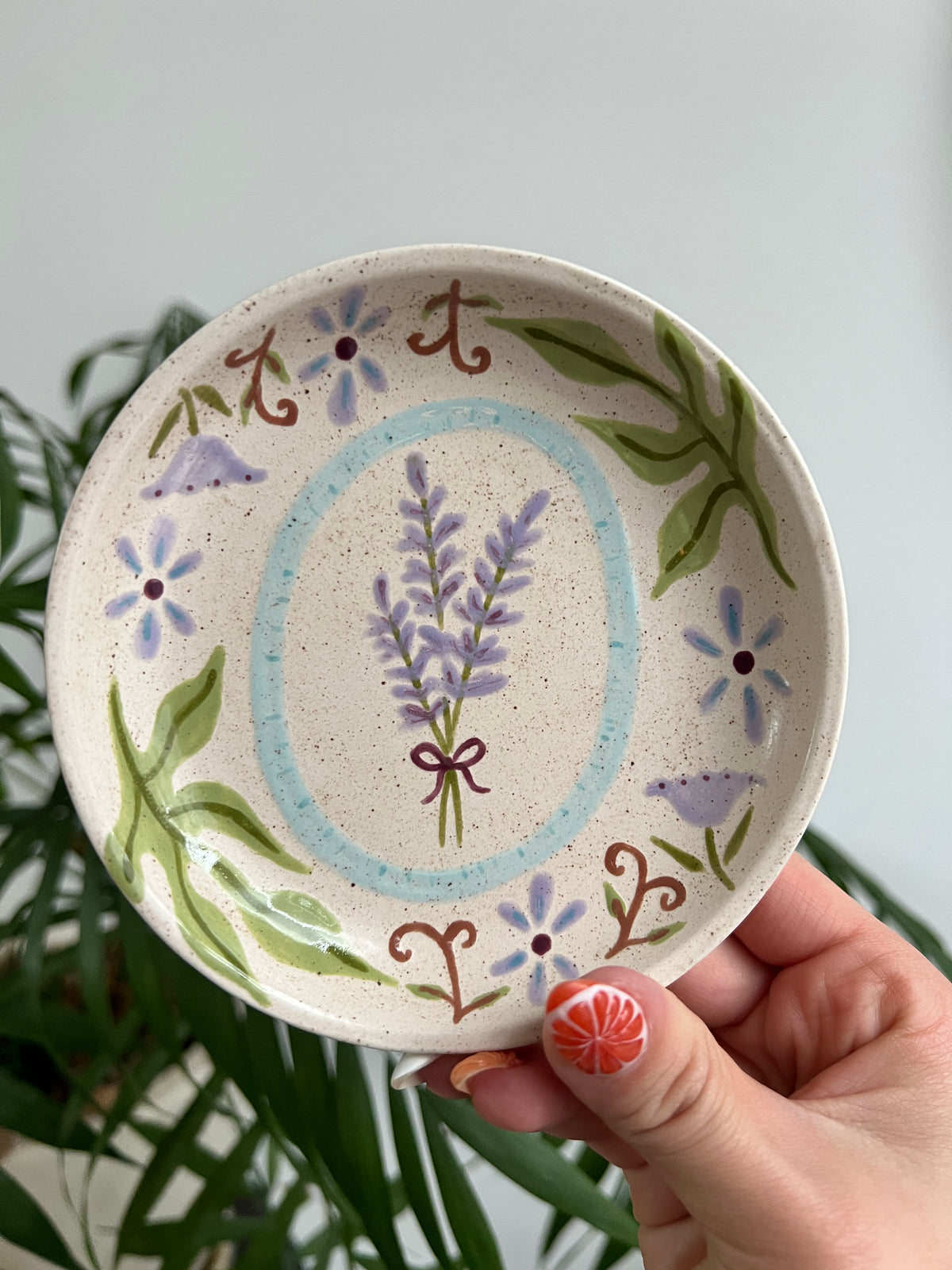 Hand holding a ceramic dish with floral design against a neutral background