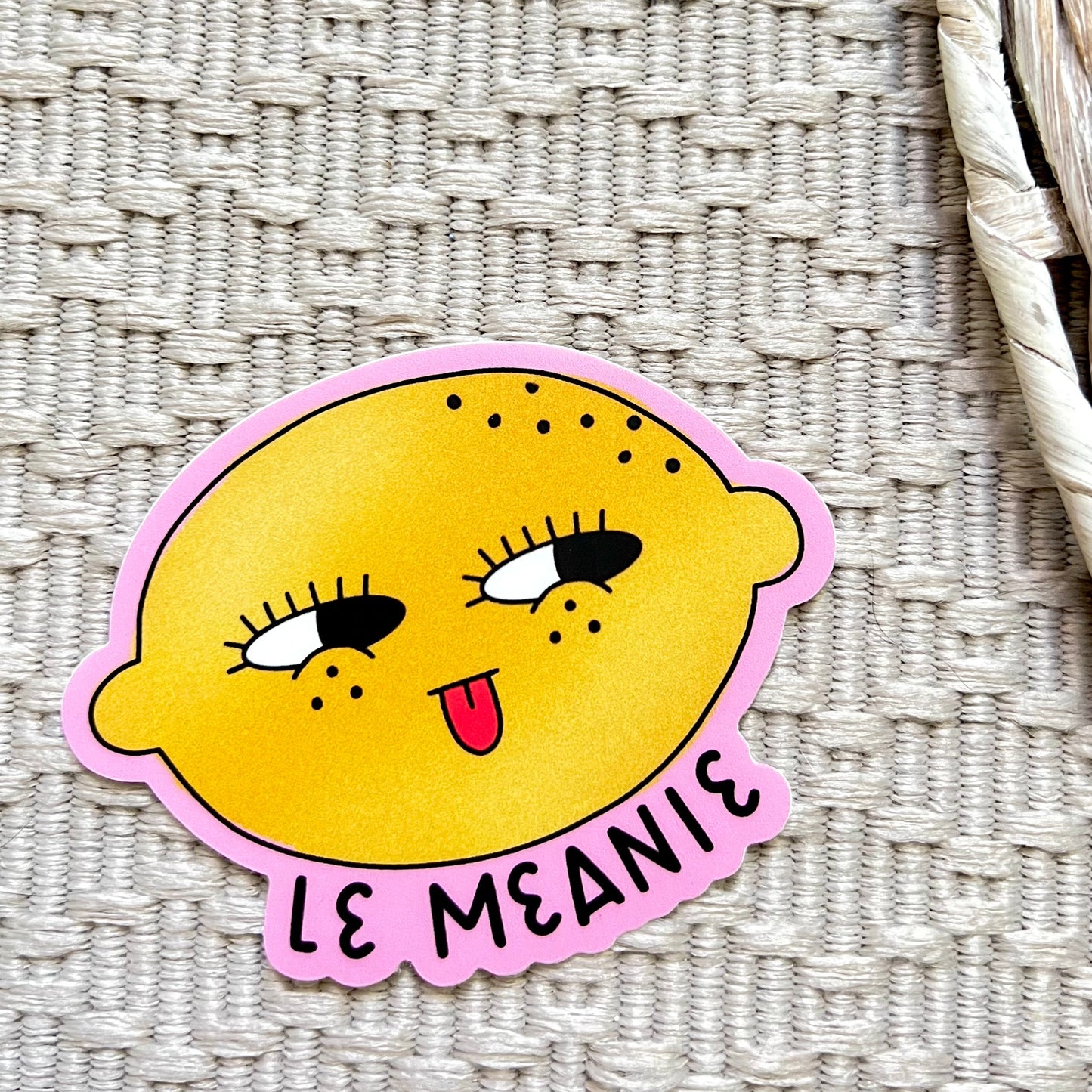 Sticker with a lemon character and 'Le Meanie' text on a textured surface