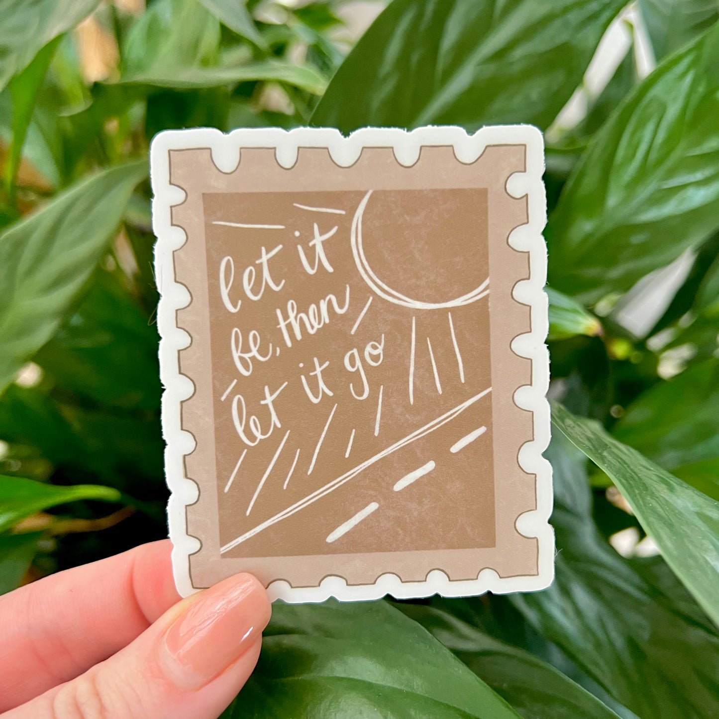 Sticker with 'let it be, then let it go' text  on a stamp shape illustration held in front of green leaves