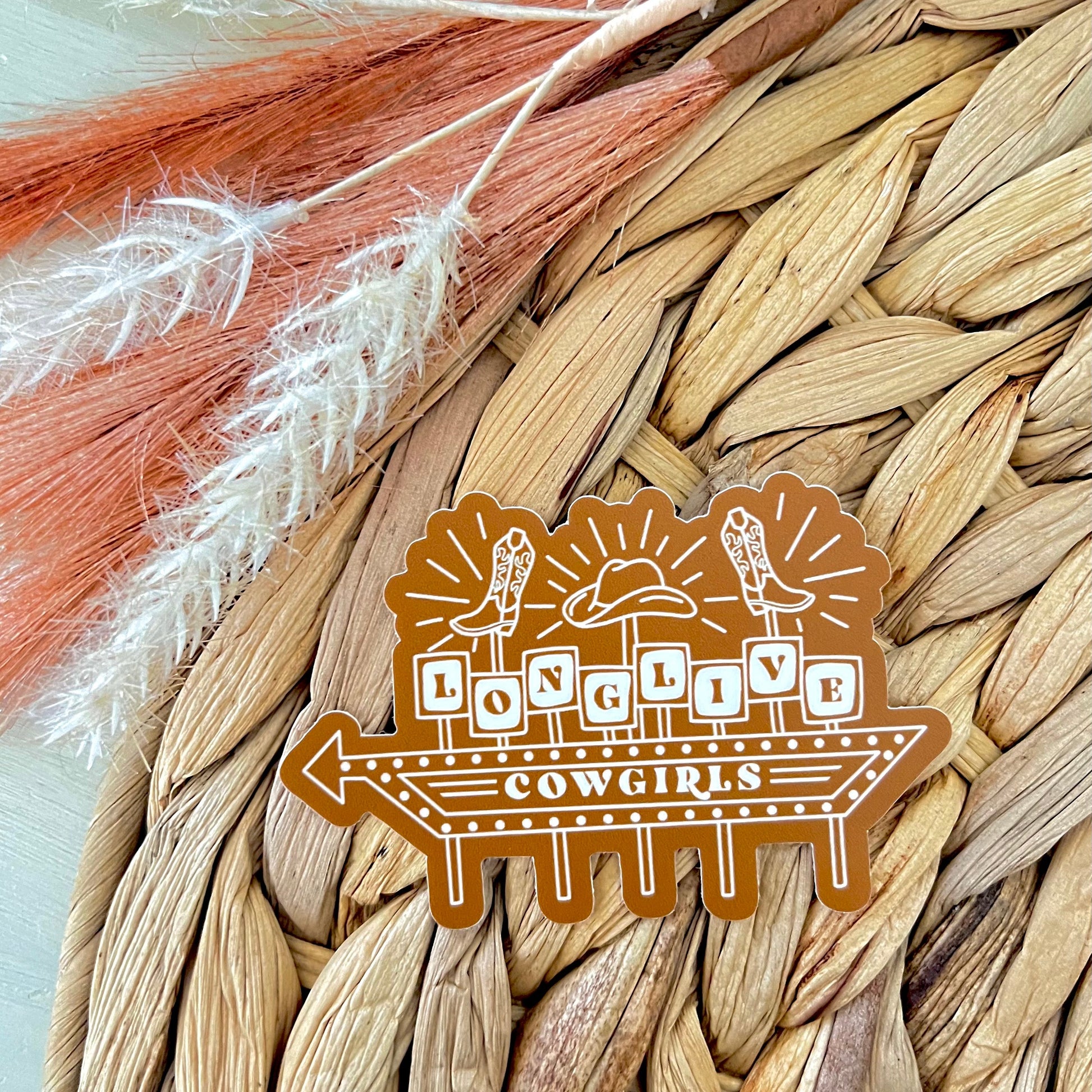 Sticker of a retro sign with 'Long Live Cowgirls' design on a woven surface.