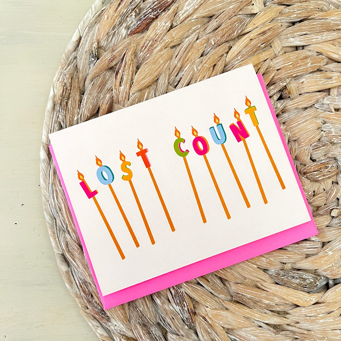 Card with colorful birthday candles spelling 'Lost Count' on a woven mat