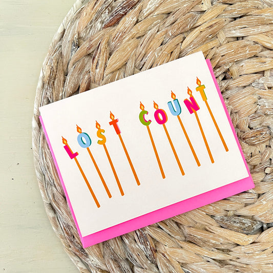 Card with colorful birthday candles spelling 'Lost Count' on a woven mat