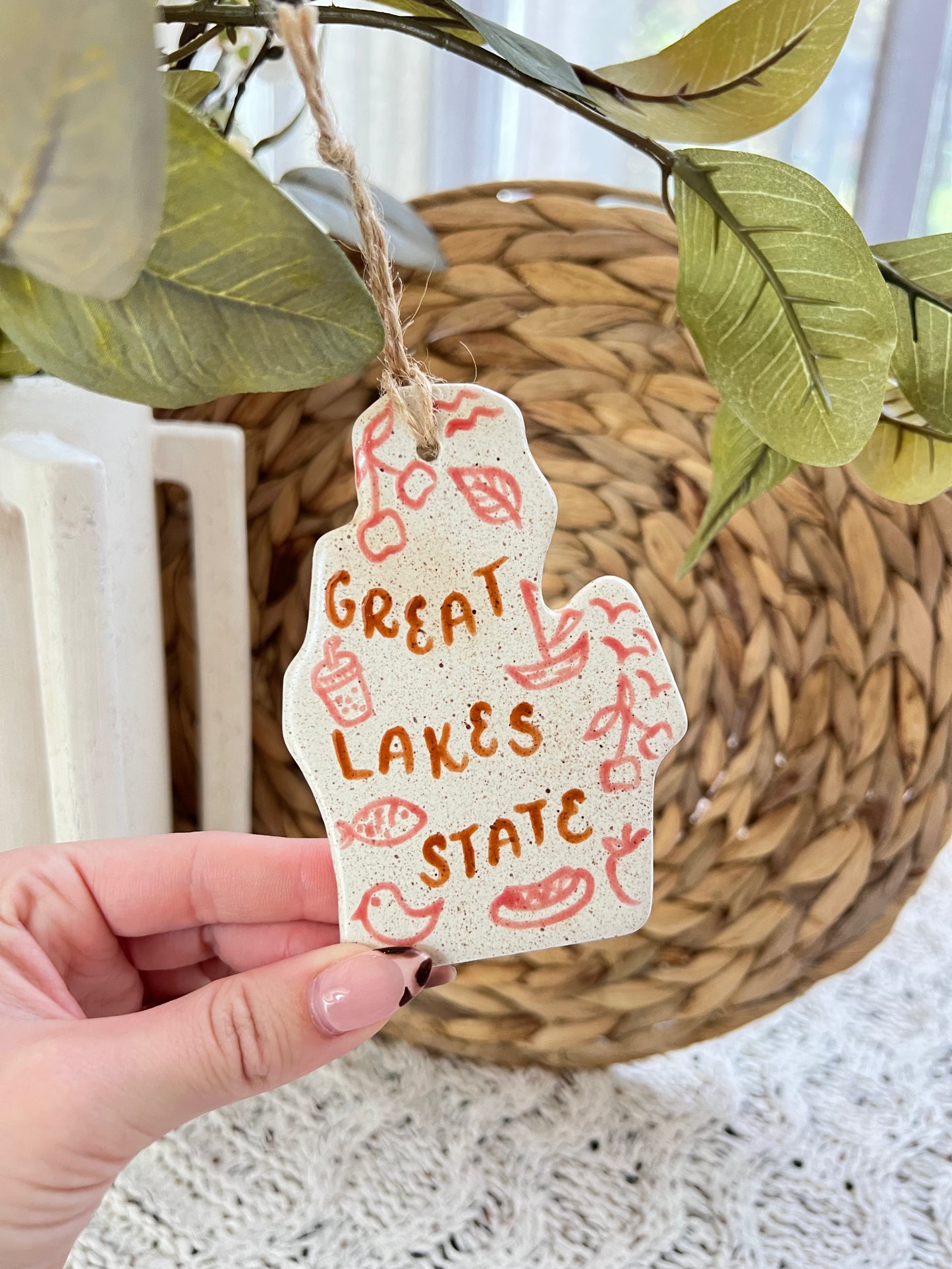 Hand holding up ornament shaped like state of Michigan that says "Great lakes state"