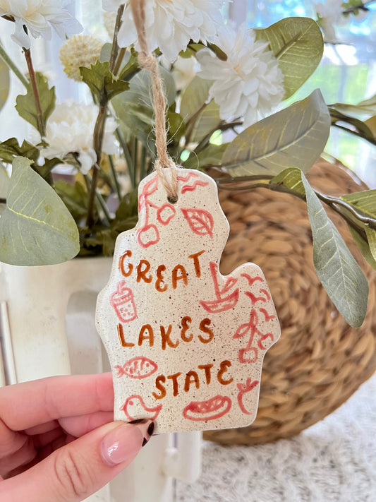 Decorative ceramic ornament with 'Great Lakes State' text held in front of a floral arrangement.