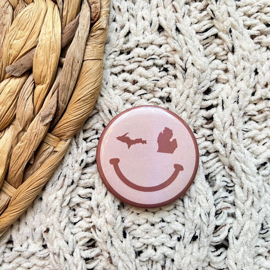 Round pink pin with smiley face design on a textured surface