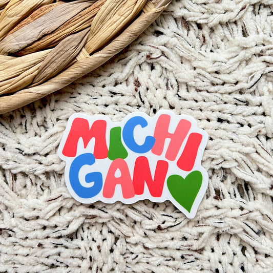 Colorful 'Michigan' sticker on a textured surface with woven object