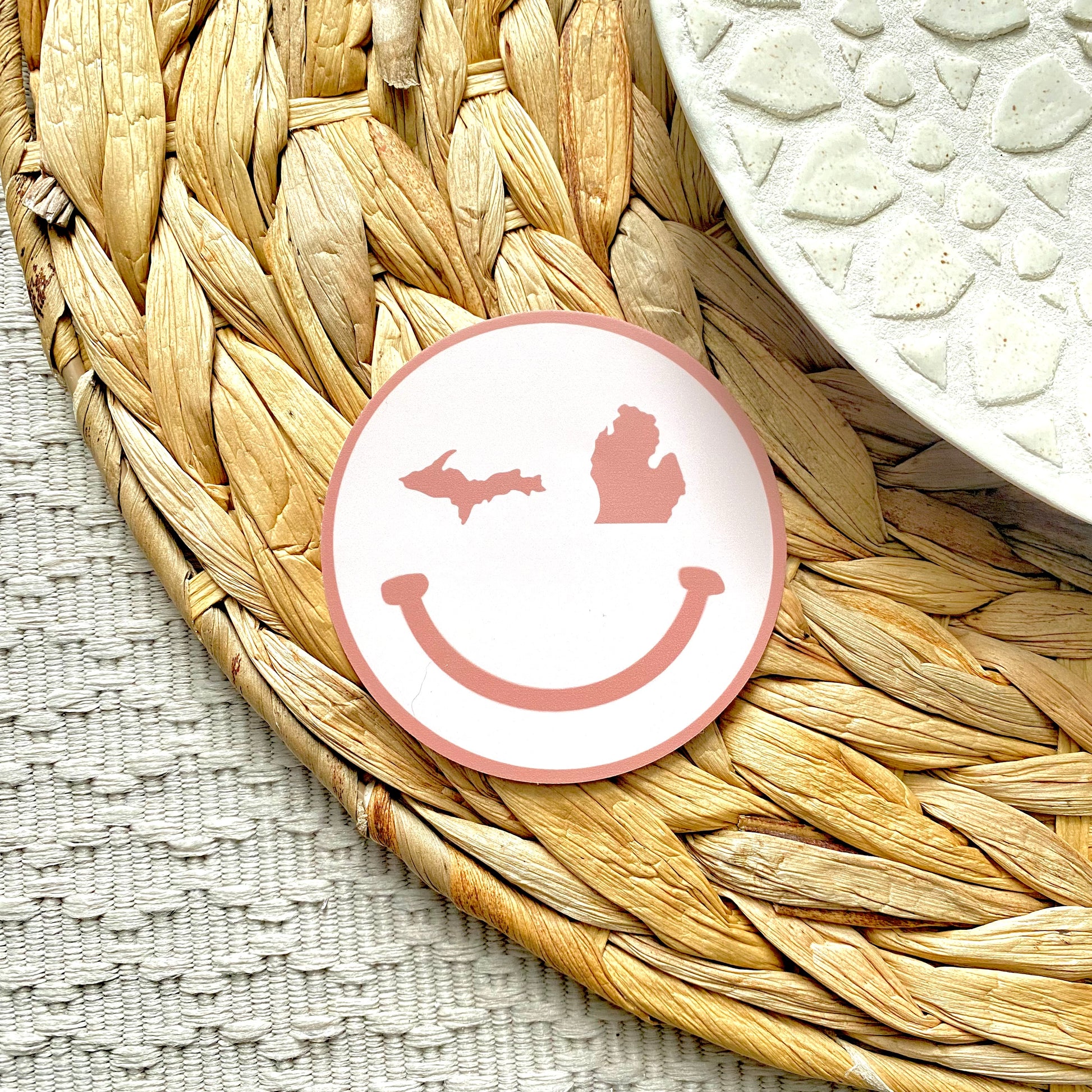 Round pink smiley face sticker on a woven mat