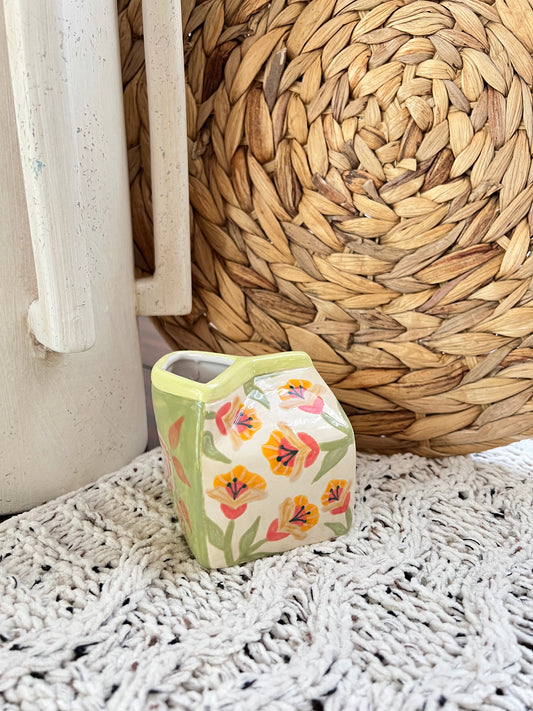 Small floral-patterned ceramic vase on a textured surface with woven basket in the background