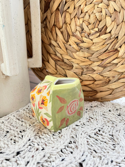 Milk Carton shaped ceramic vase with floral design on a textured surface