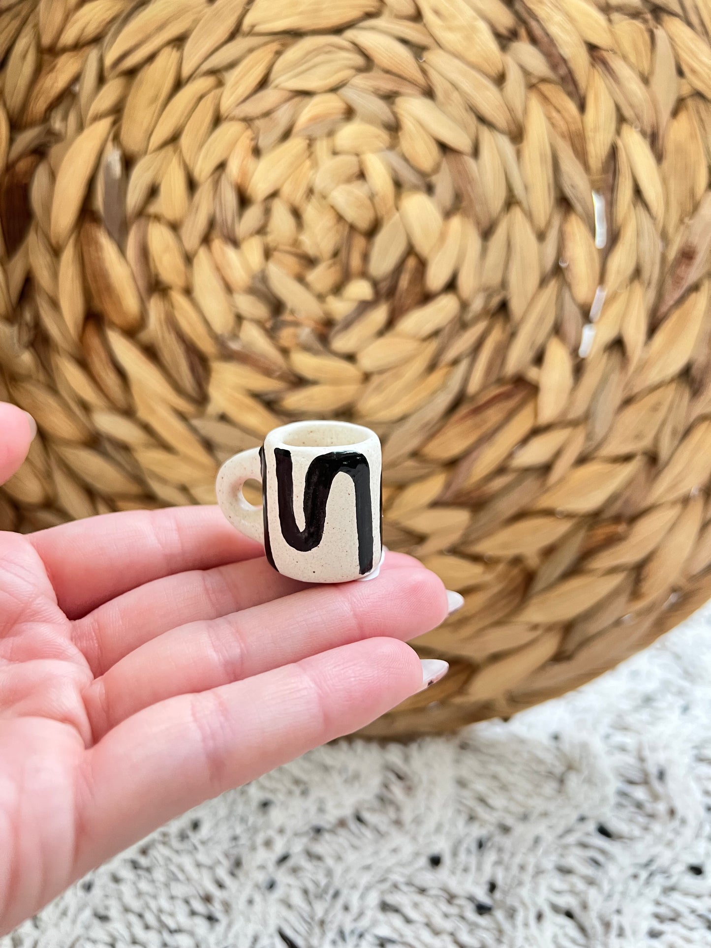 Small ceramic mug with a black abstract pattern on a hand against a woven basket background