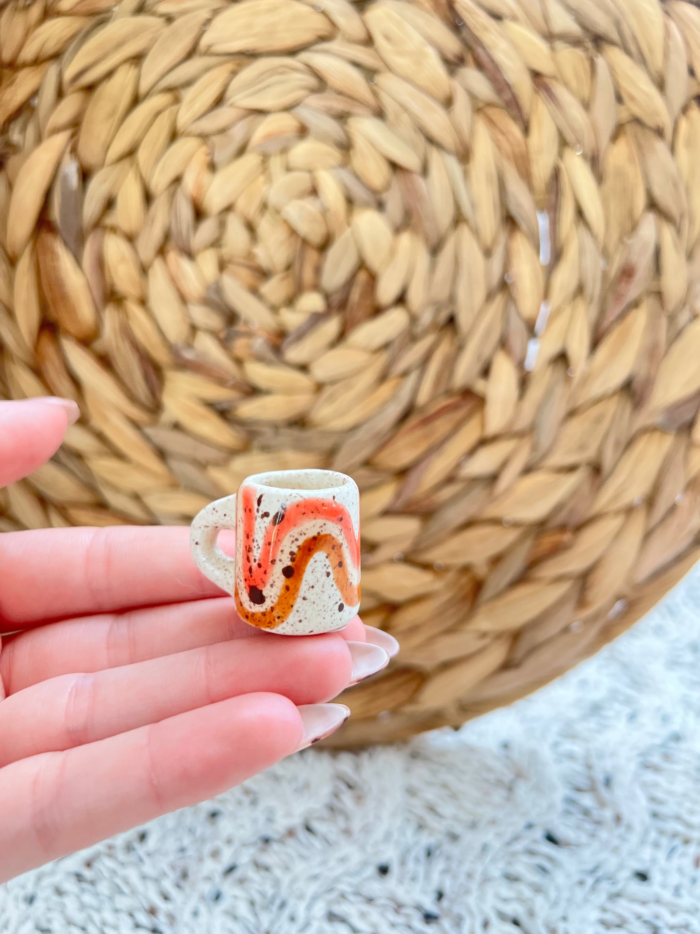 Small ceramic cup with abstract design held in a hand against a woven mat background