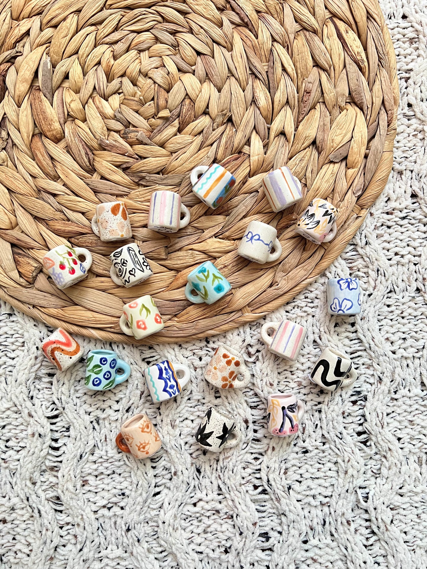 Collection of small ceramic mug-shaped trinkets on a woven mat