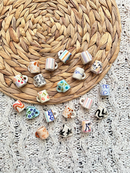 Collection of small ceramic mug-shaped trinkets on a woven mat