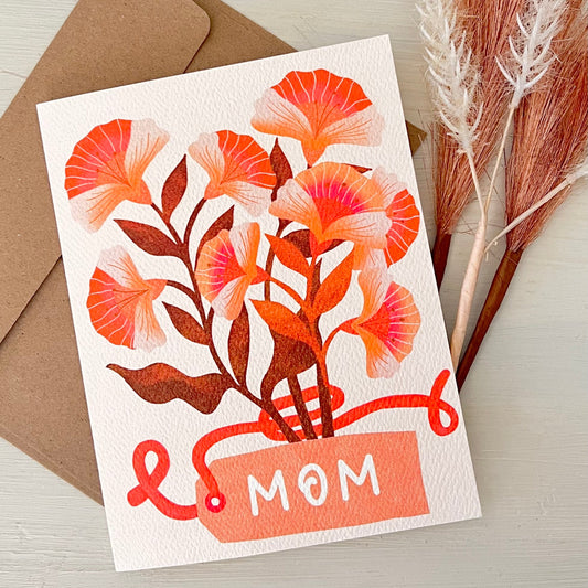 Greeting card with floral design and 'Mom' text on a wooden surface