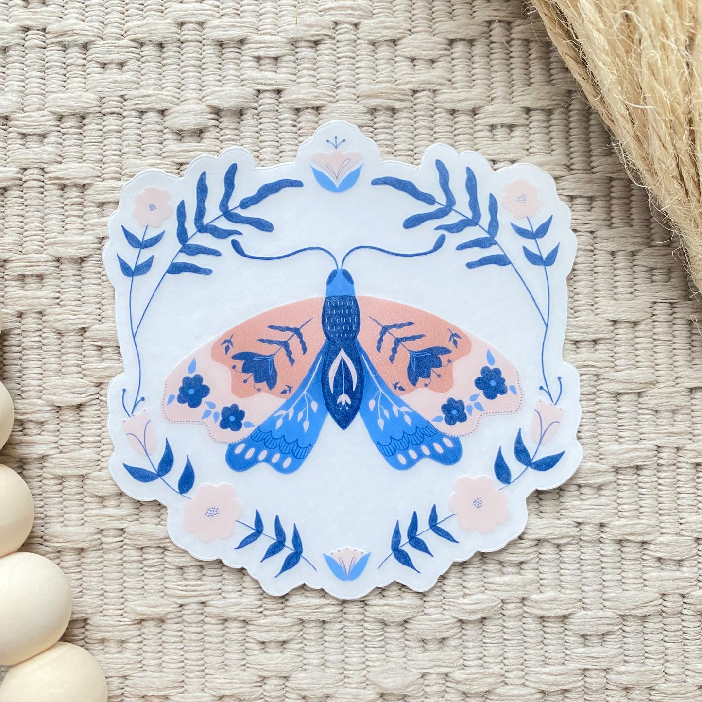 Decorative sticker with a floral blue and pink moth design on a woven surface
