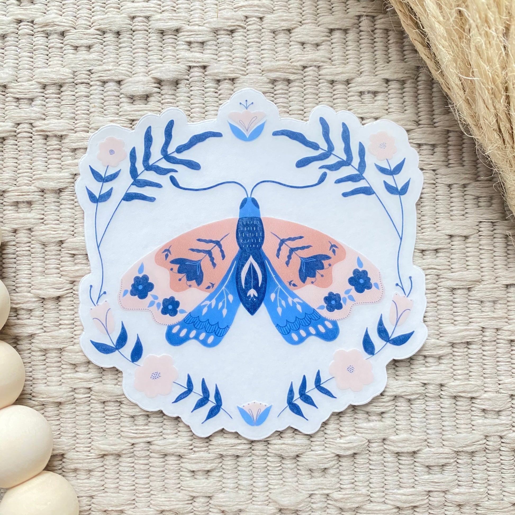 Decorative sticker with a floral blue and pink moth design on a woven surface